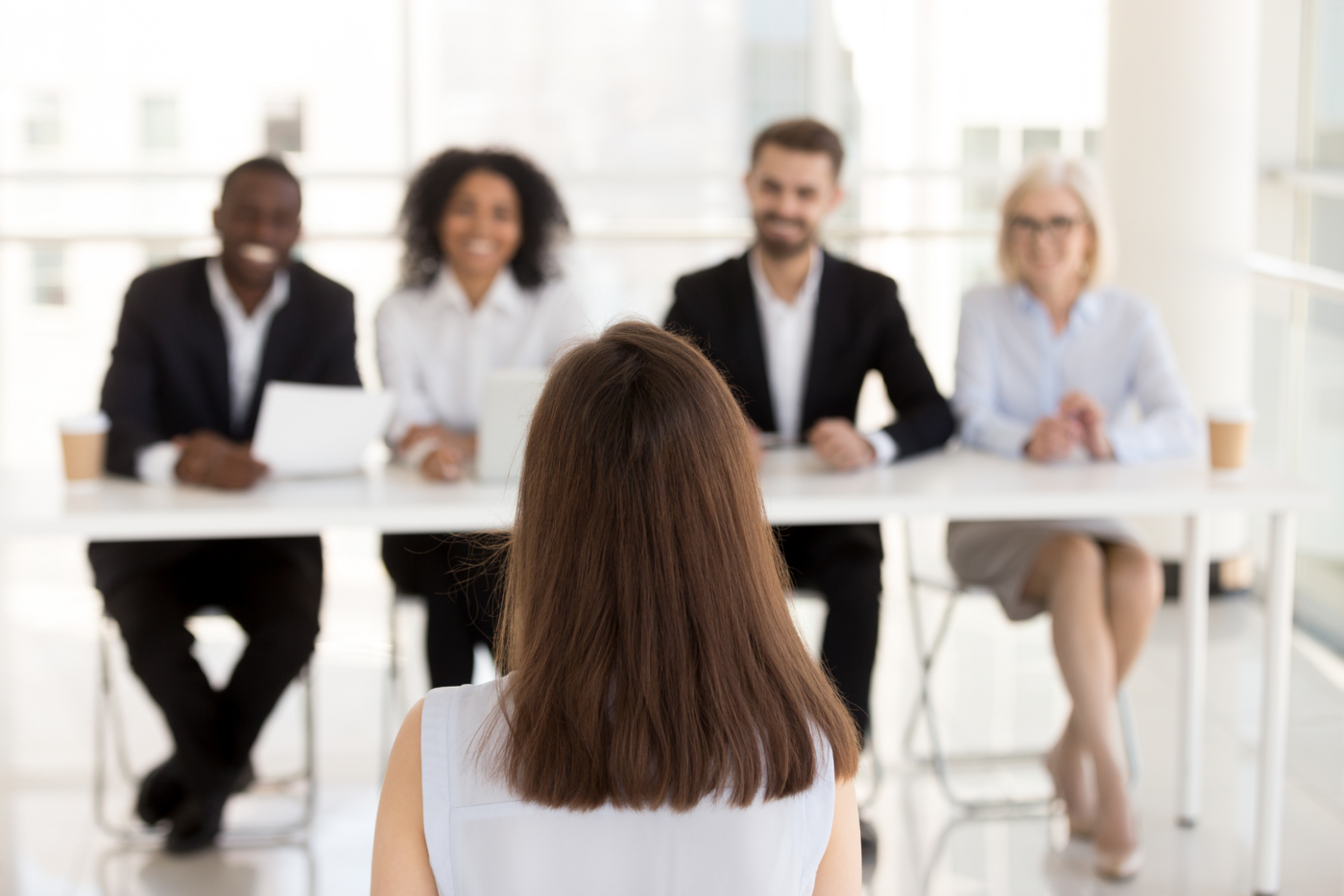 Junge Kandidatin beim Vorstellungsgespräch mit vier freundlichen Interviewern in einem hellen Büro.