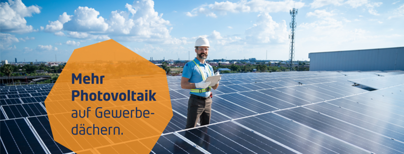 Mann mit Helm und Klemmbrett steht auf einem Gewerbedach voller Solarmodule.